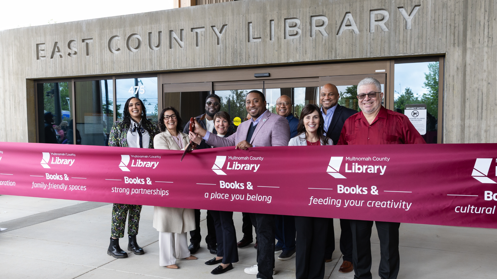 Photo of Multnomah County officials cutting a ceremonial ribbon beneath the concrete "East County Library" sign