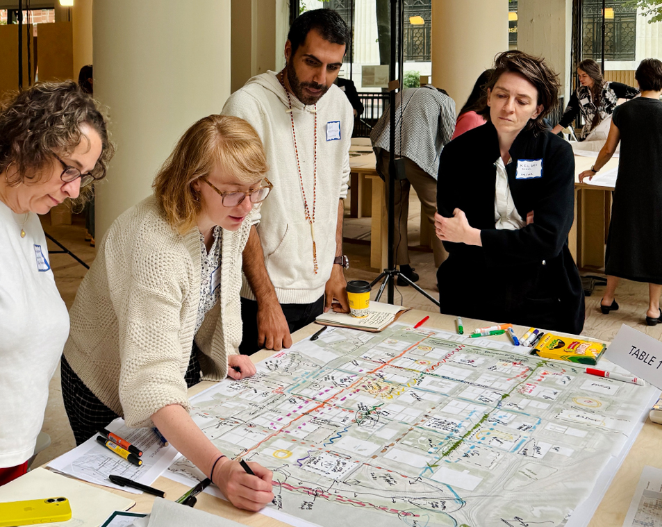 A large map of downtown Portland is laid on a work table with trace paper over it. A group of urban designers gather with Mayer/Reed Associate Principal Shannon Simms, using markers to brainstorm ideas for new street connections in downtown Portland.