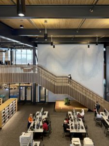 Photo of staircase and wall graphic at Moorhead Public Library. In the foreground, people are working at computers.
