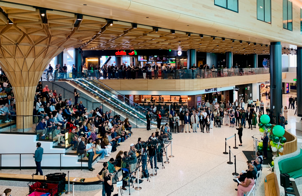 People and press fill the stadium seats beneath the signature wood ceiling during the ribbon cutting ceremony for the C Concourse expansion.