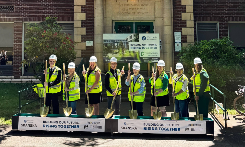 A group of eight people post for a ceremonial groundbreaking at Portland's Cleveland High School. They are wearing hard hats, safety vests and holding golden shovels.