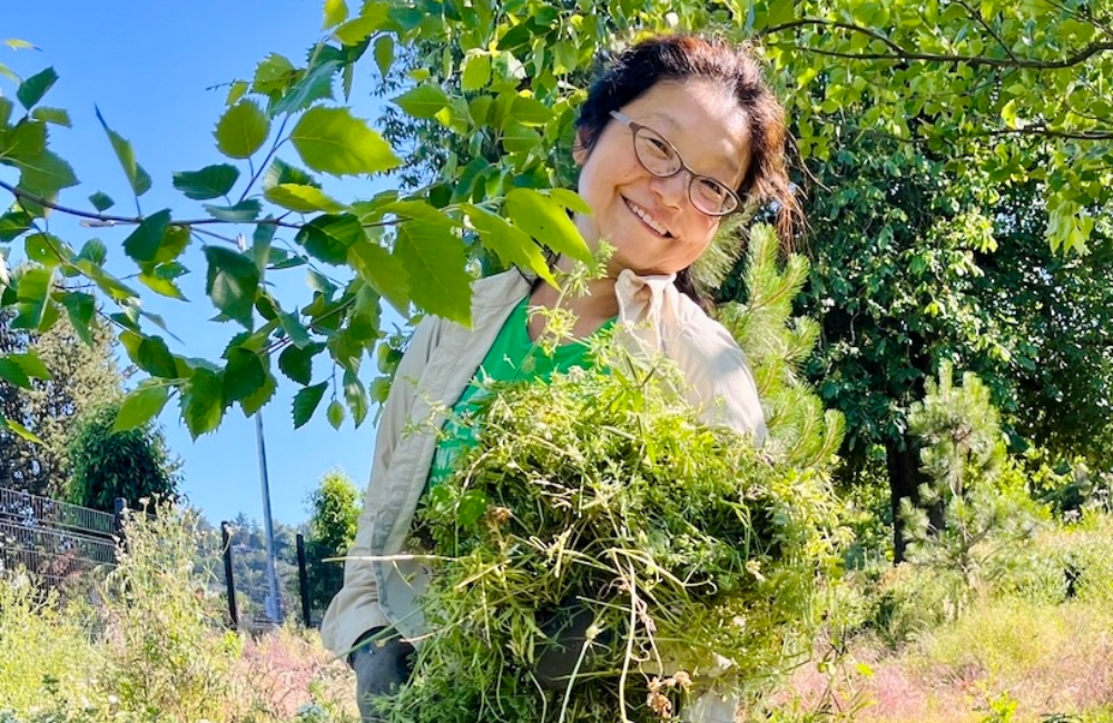 A smiling volunteer holding the weeds she removed from the planting area