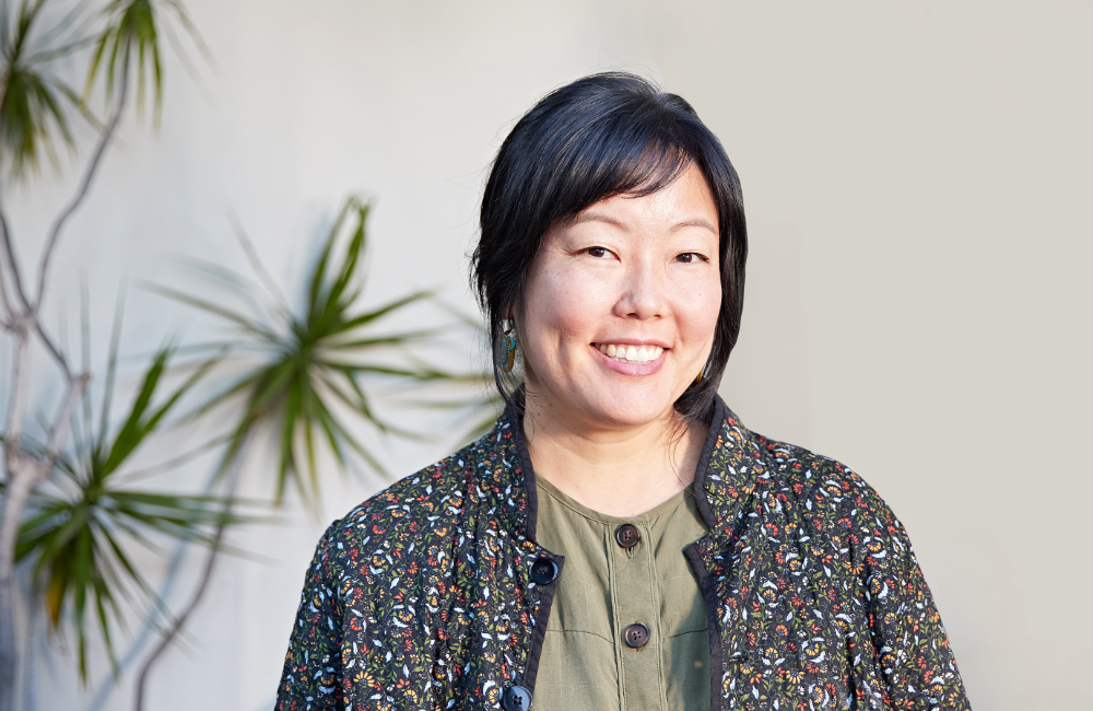 Headshot of Associate Emily Morishita in front of a white wall with a plant in the background