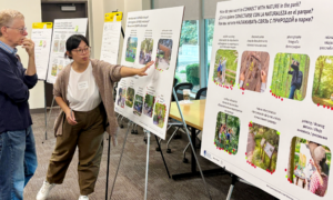 A Mayer/Reed landscape architect stands with an east Vancouver community member and points at the multilingual display boards at a community engagement event. The boards display images of different types of programming and park uses.